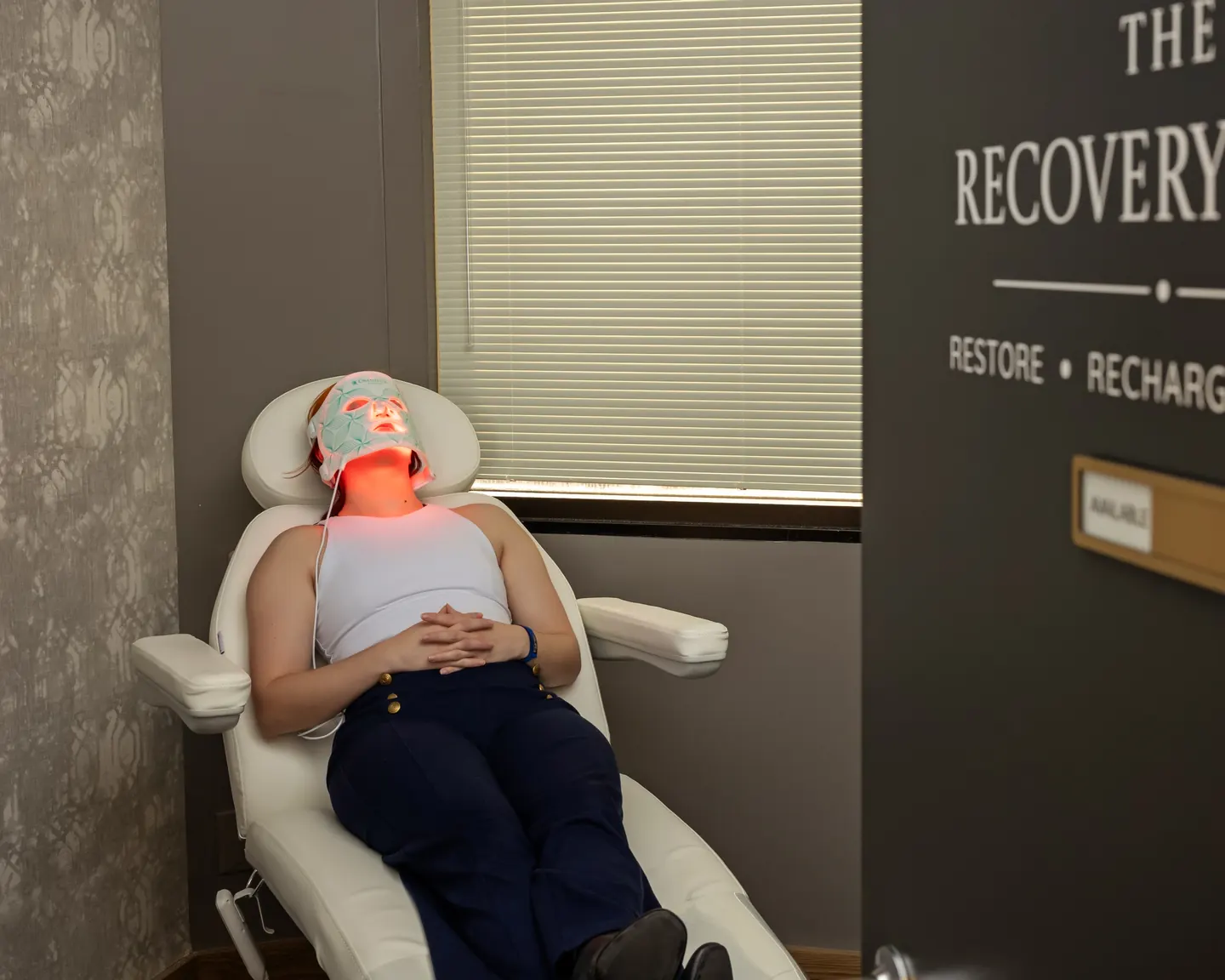 A patient relaxing in the Recovery Suite under a red LED light therapy face mask